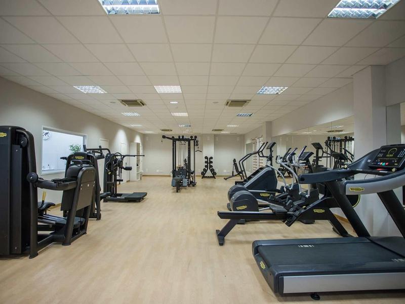 Heller Fitnessraum mit Laufbändern, Kraftgeräten und Holzfußboden unter deckenleuchten.