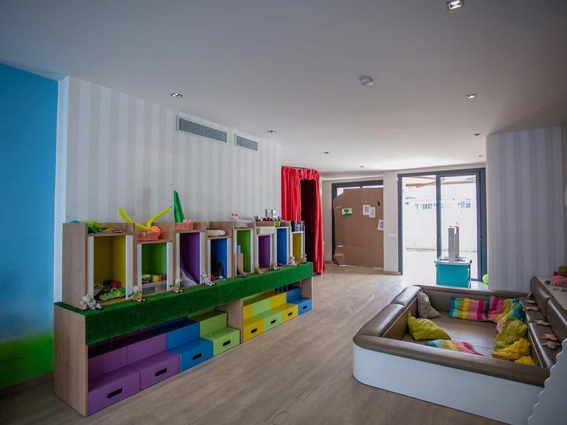 Kinderspielzimmer mit bunten Regalen, Sitzkissen und heller Holzbodenbeleuchtung.
