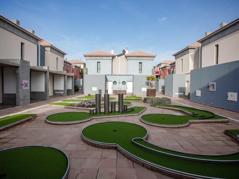 Ein kleiner Minigolfplatz mit grünen Bahnen zwischen modernen weißen Mehrfamilienhäusern.