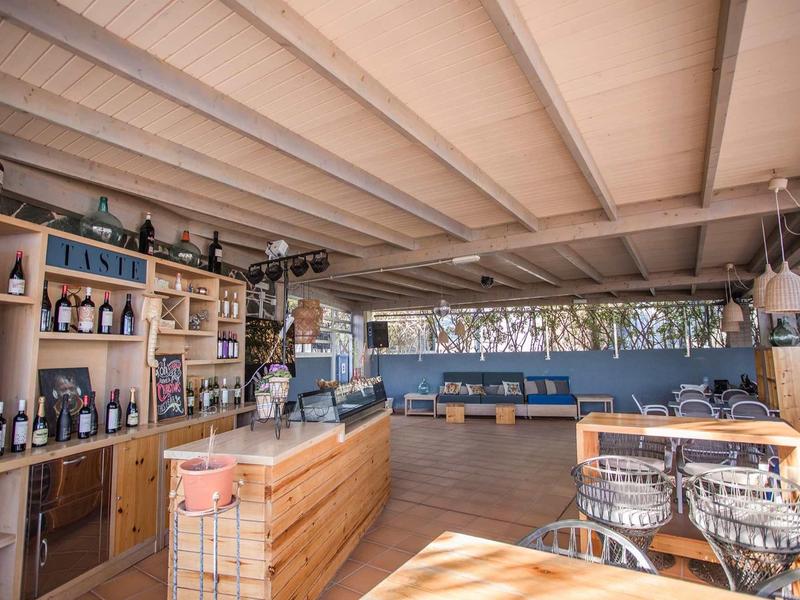 Moderner Gastraum mit Holzmöbeln, Weinregal links, blauem Sitzbereich und großen Fenstern.