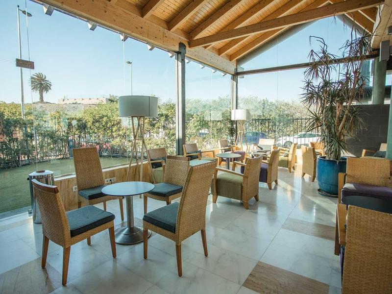 Modernes Café mit Holzdach, Glaswänden, Stühlen aus Holz und Kugeltischen bei Tageslicht.