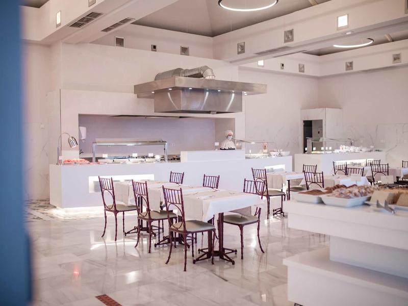 Heller, leerer Gastraum mit weißen Wänden, glänzendem Boden und mehreren Tischen mit Stühlen.