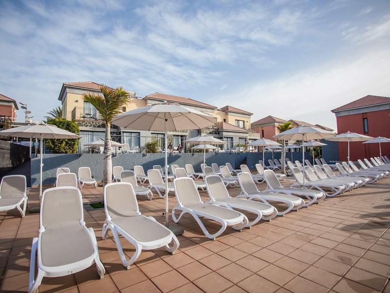 Leere weiße Liegestühle und Sonnenschirme auf einer Hotelterrasse unter blauem Himmel.