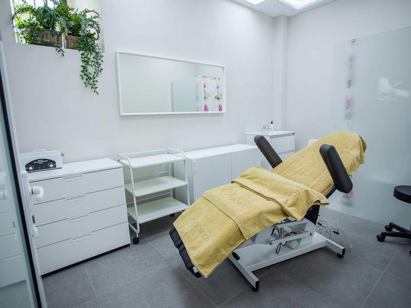 Heller Behandlungsraum mit verstellbarem Behandlungstisch, Schubladen und Pflanzen an der Wand.