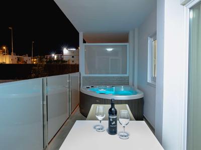 Balcony at night with a hot tub, a bottle of wine, and two glasses on a white table.