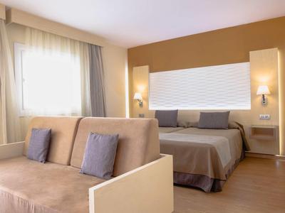 Modern hotel room with double bed, sofa, and warm tones.