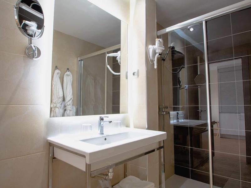 Salle de bain moderne avec lavabo, miroir et porte de douche en verre dans des tons chauds.