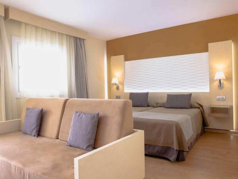 Chambre d'hôtel moderne avec lit double, canapé et tons chauds.