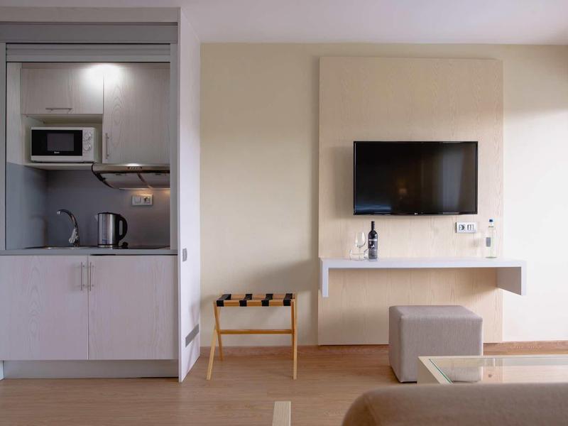 Espace chambre d'hôtel moderne avec kitchenette intégrée, télévision et coin salon.