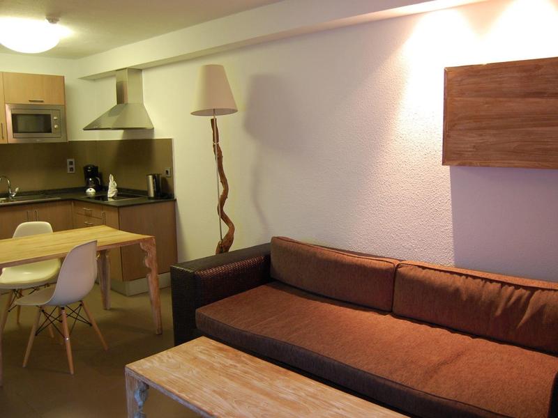 Kleines Wohn- und Küchenzimmer mit braunem Sofa, Holztisch, Esstisch und weißen Stühlen.