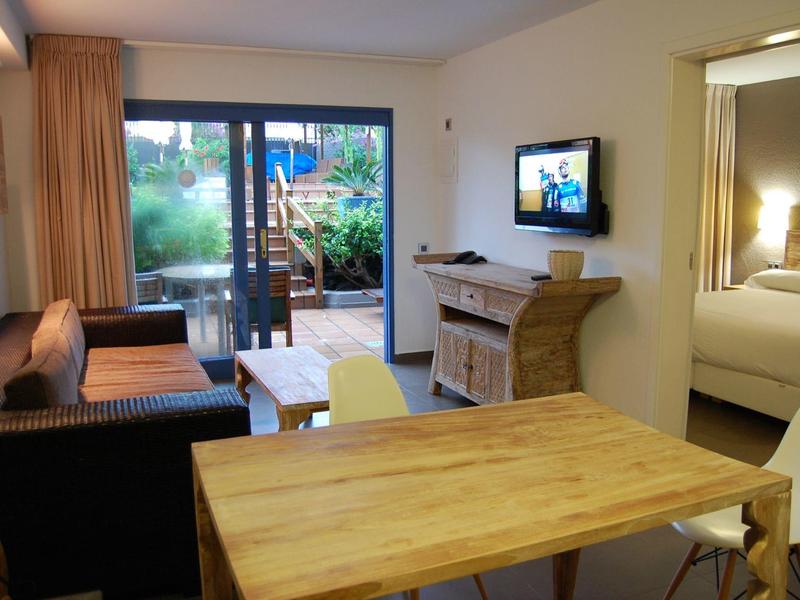 Helles Wohnzimmer mit Holztisch, Sofa, Fernseher und Zugang zum Garten mit Terrasse.