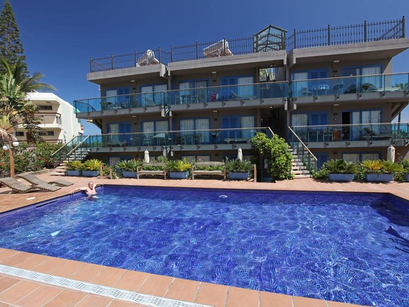 Moderne Hotelanlage mit großem beheiztem Pool, Sonnenliegen und Glasbalustraden bei klarem Himmel.