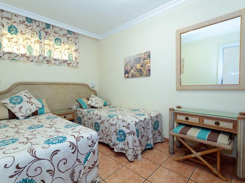 Chambre double avec dessus de lit colorés, miroir au-dessus d'une commode et rideau à motifs.