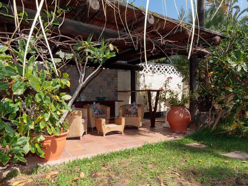 Patio couvert avec chaises et tables entouré de plantes et d'herbe.
