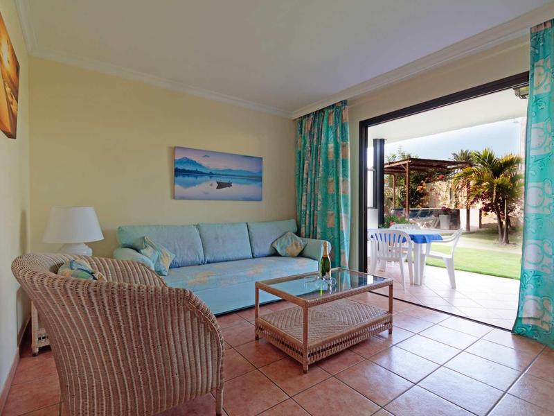 Salon avec canapé et fauteuils donnant sur la terrasse et la piscine par la porte terrasse ouverte.