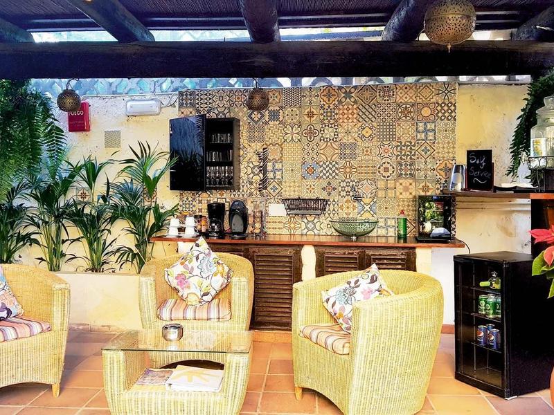 Terrasse avec des fauteuils en rotin et un mur carrelé coloré, décorée de plantes.