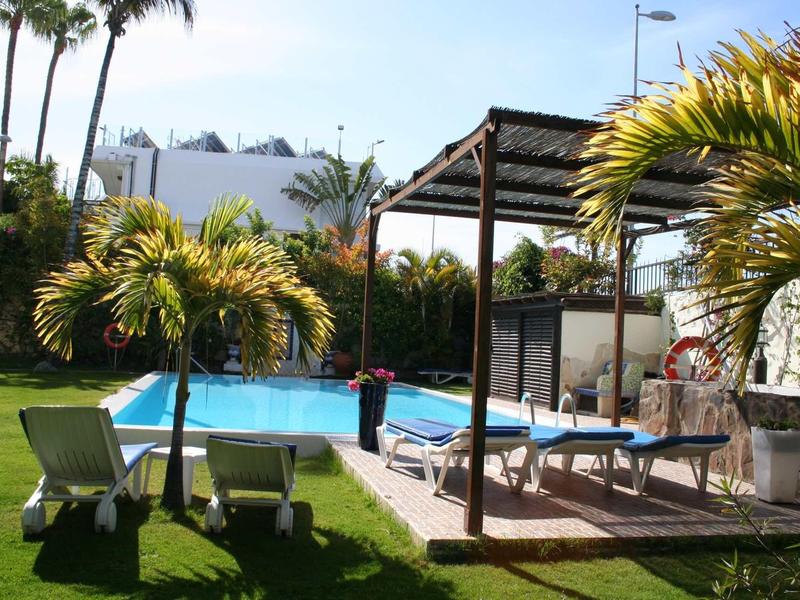Piscine avec chaises longues et structure d'ombre dans le jardin d'un hôtel par une journée ensoleillée.