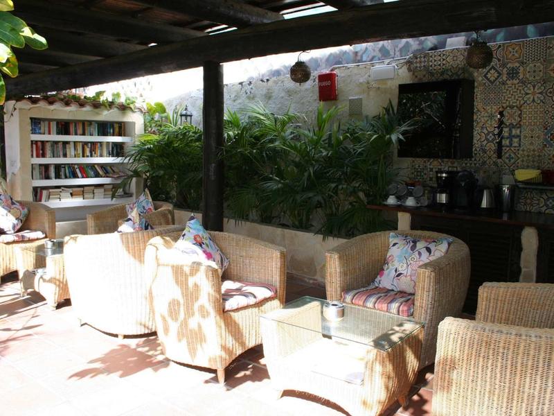 Espace extérieur couvert et confortable avec fauteuils, plantes et bibliothèque.