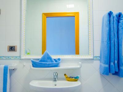 Weißes Badezimmer mit Waschbecken, großem Spiegel, zwei blauen Handtüchern und einer Banane.