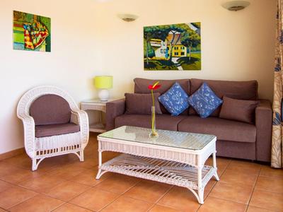 Helles Wohnzimmer mit braunem Sofa, weißem Sessel, Glas-Couchtisch und bunter Wanddekoration.