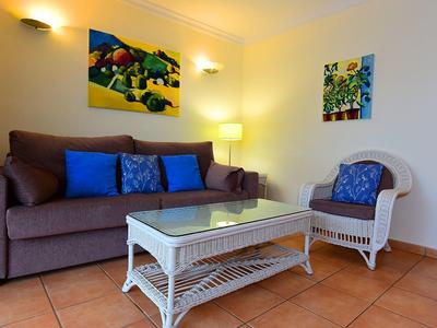 Gemütliches Wohnzimmer mit braunem Sofa, blauem Kissen, weißen Rattanstuhl und Glas-Couchtisch.