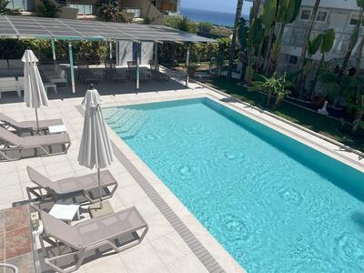 Ein klarer blauer Pool mit weißen Liegestühlen und geschlossenen Sonnenschirmen umgeben von Gebäuden.