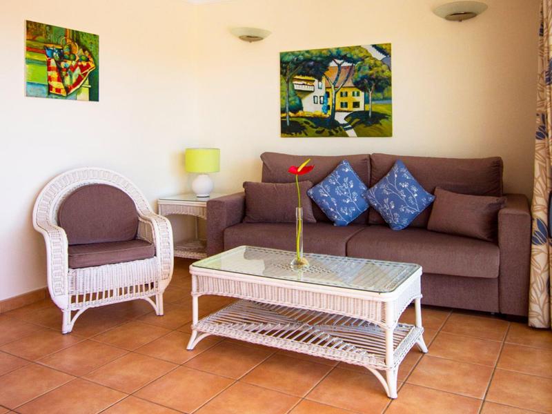 Helles Wohnzimmer mit braunem Sofa, weißem Sessel, Glas-Couchtisch und bunter Wanddekoration.