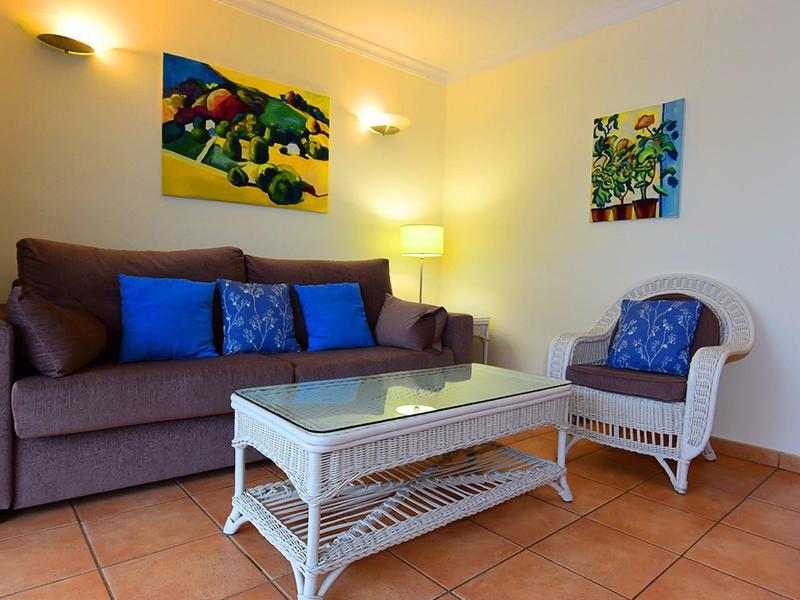 Gemütliches Wohnzimmer mit braunem Sofa, blauem Kissen, weißen Rattanstuhl und Glas-Couchtisch.