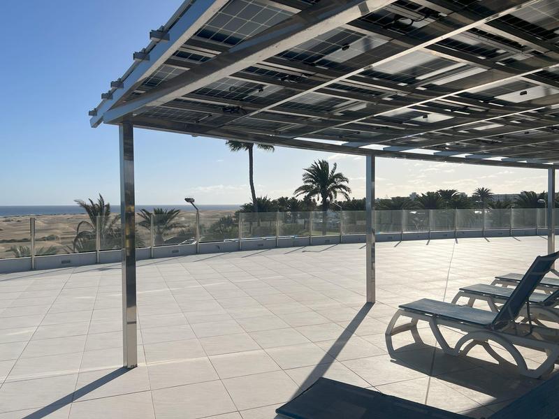 Große Terrasse mit weißen Fliesen, Sonnenliegen und Glasgeländer mit Blick auf Palmen und Meer.