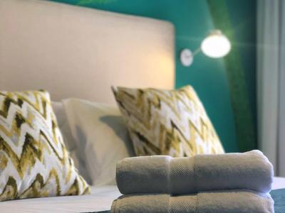 Ein gemütliches Bett mit zwei gemusterten Kissen, weißen Handtüchern und grüner Wand mit Pflanzenmuster.