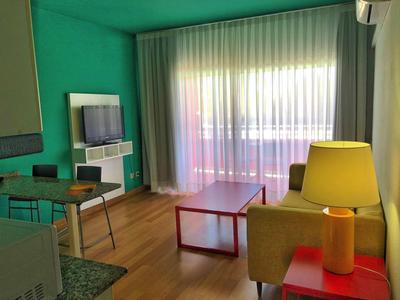 Helles Wohnzimmer mit grünem Akzent, Sofa, rotem Tisch, Stehlampe und großem Fenster mit Gardinen.