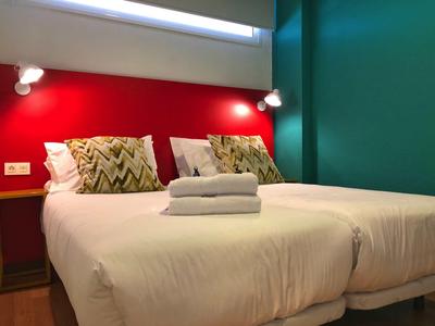 Zimmer mit zwei Einzelbetten, weißen Laken, gemusterten Kissen, roter Wand und grüner Wandfarbe.