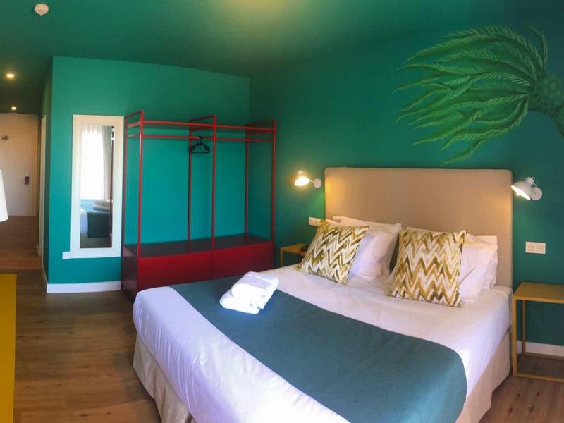 Nowoczesny pokój hotelowy z podwójnym łóżkiem, zieloną ścianą akcentową i dużym lustrem.