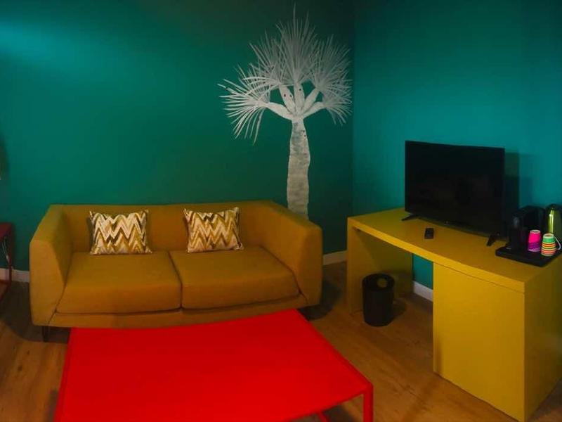 Przytulny salon z pomarańczową sofą, kolorowym fotelem i czerwonym dywanem w ciepłym świetle.