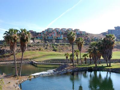 Terreno verde da golf con palme e case sullo sfondo sotto un cielo azzurro.