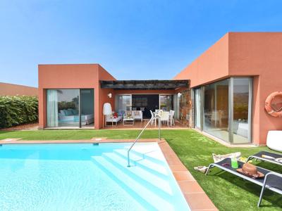 Casa vacanze moderna con grande piscina e lettini in giardino sotto un cielo sereno.