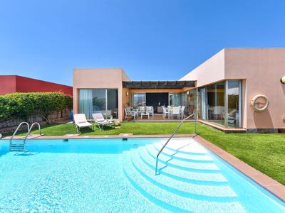 Bungalow moderno con piscina e sdraio sotto un cielo azzurro limpido