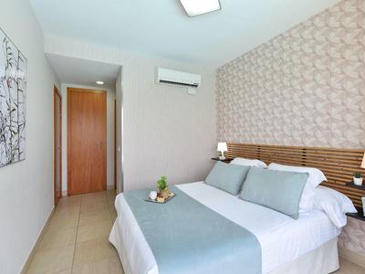 Helles Schlafzimmer mit Doppelbett, hellblauer Bettwäsche, Holzakzenten und Tapetenmuster an der Wand.