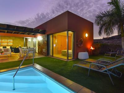 Modernes Haus mit Pool, Terrasse, Liegestühlen und Palmen bei Sonnenuntergang.