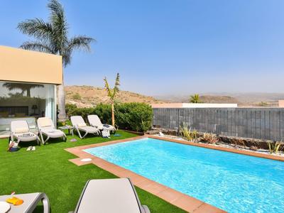 Moderner Außenbereich mit rechteckigem Pool, Liegestühlen, grünem Kunstrasen und Palmen vor klarem Himmel.