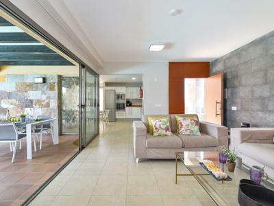 Moderner Wohnraum mit grauen Sofas, Glastisch, Terrassentüren und heller Fliesenboden.