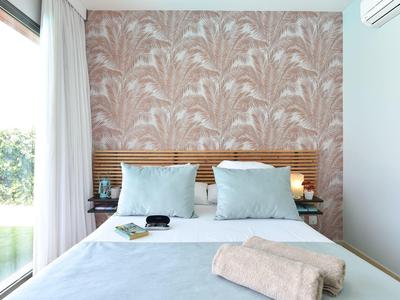 Schlafzimmer mit hellblauem Bettzeug, gemusteter rosa Tapete und großen Glasfenstern.