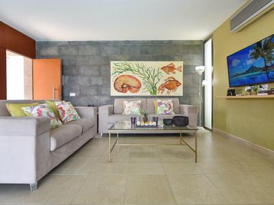 Moderner Wohnraum mit grauer Couch, Glas-Couchtisch, Wandkunst und großem Fernseher an grüner Wand.