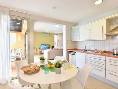 Moderne helle Küche mit runder weißer Tisch und weißen Stühlen, offen zum Wohnzimmer mit Sofa.