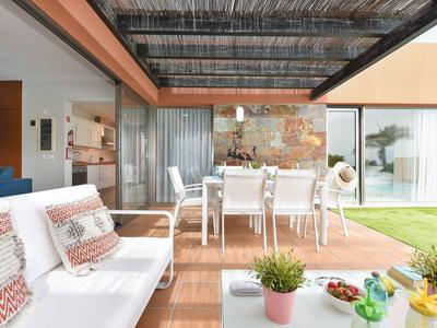 Moderne Terrasse mit weißen Möbeln, Holzboden, Pflanze und Blick auf grünen Garten.