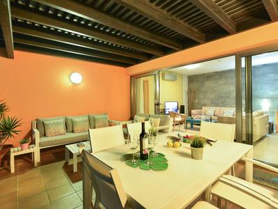 Überdachter Balkon mit orangefarbenen Wänden, Tisch, Stühlen, Sofa und grünen Pflanzen.