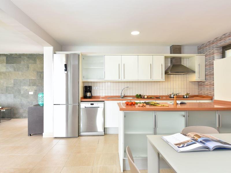 Helle Küche mit weißen Schränken, großer Insel, Holzanrichte und Edelstahlgeräten.