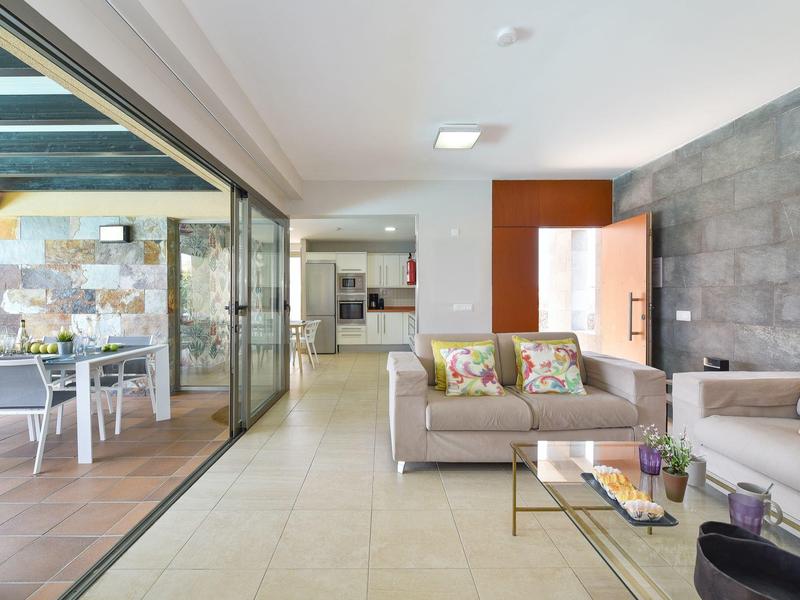 Moderner Wohnraum mit grauen Sofas, Glastisch, Terrassentüren und heller Fliesenboden.