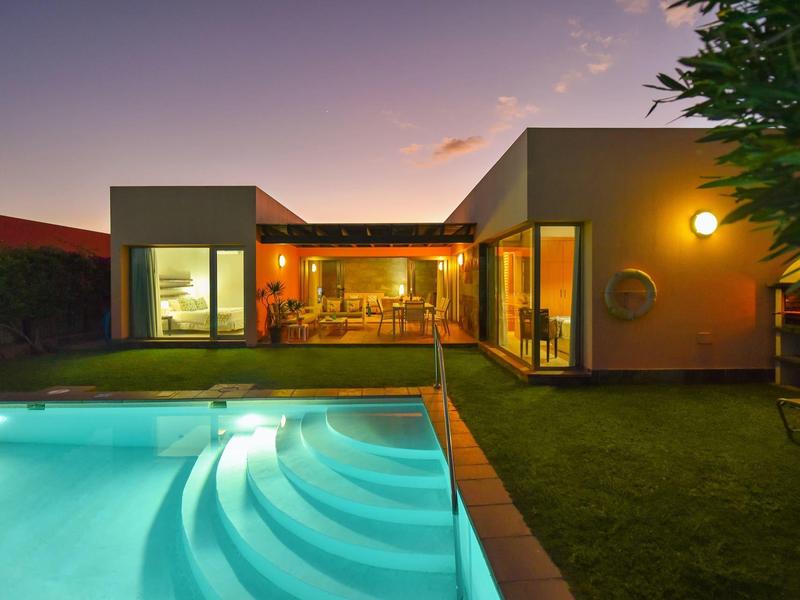 Modernes Haus mit großen Fenstern, beleuchtetem Pool und gepflegtem Garten bei Dämmerung.