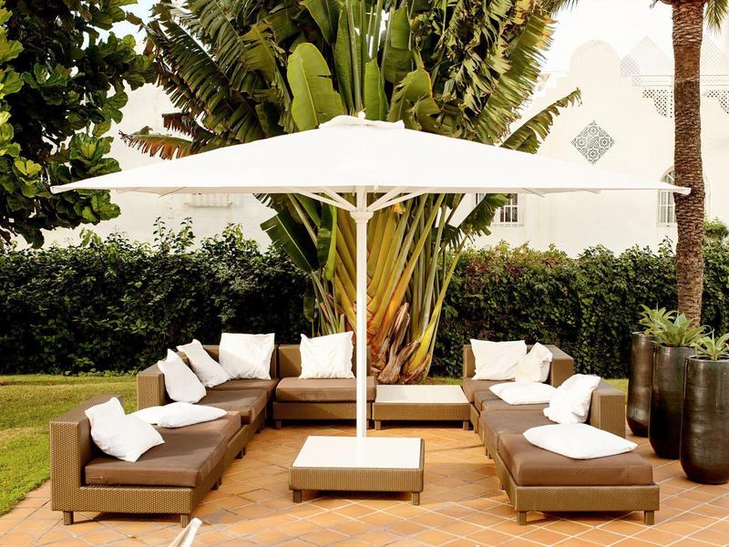 Gemütliche Outdoor-Lounge mit braunen Sofas, weißen Kissen und großem weißem Sonnenschirm.